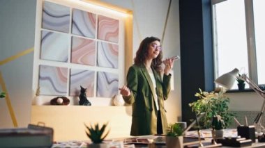 Kendine güvenen iş kadını modern ofisteki akıllı telefondan sesli mesaj kaydediyor. Başarılı bir kadın yönetici iş yerindeki sesli mesajlar için akıllı telefon kullanıyor. Hoparlörden konuşan çekici bir kız.