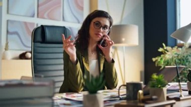 İş yerinde telefonla konuşan ciddi profesyonel bir kadın. Çekici özgüvenli ofis yöneticisi, modern kabinede iş meselelerini tartışan ortakları arıyor. Zeki iş kadını konuşuyor..