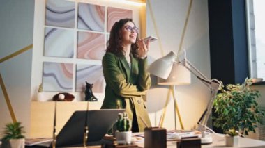 Güzel yaratıcı iş kadını akıllı telefondan sesli mesaj kaydediyor. Ofis işi için sanal asistan uygulaması kullanan meşgul bir kız. Hoparlörden konuşan genç bir iş kadını..