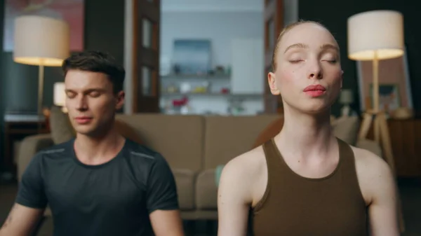 Stock image Millennial family practicing breathing exercises sitting in lotus pose at home closeup. Blond wife making yoga asana with husband sitting on floor. Young couple with closed eyes meditating together.