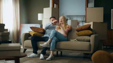 Yeni evden gülümseyen kadına anahtar hediye eden tatmin olmuş genç bir adam. Karton kutuların yanında rahat koltukta oturan mutlu çift yeni dairenin tadını çıkarıyor. Neşeli aile kiralık ev.