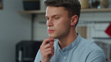 Yakın plan genç adam ev mutfağında otururken işini düşünüyor. Kariyer beklentilerini düşünen düşünceli bir adam. Evde tek başına çalışan çekici bir serbest yazar. Uzaktan çalışan çözme sorunları.