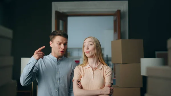 Young unhappy family conflicting at home close up. Angry nervous husband squabbling disappointed blond wife in room full of closed boxes. Couple quarrel about misunderstanding in relationship.