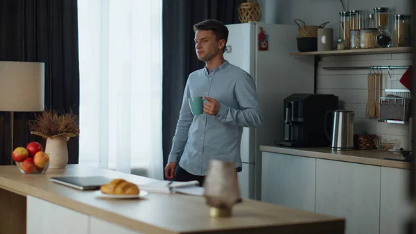 Confident man start work on modern laptop sitting at kitchen table with fresh coffee. Young freelancer opening computer to check email in morning. Attractive businessman preparing remote workplace.