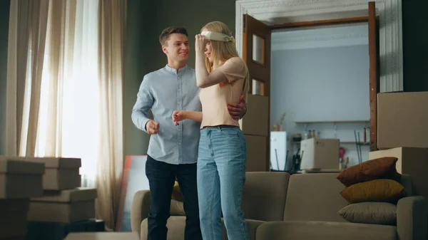 Successful young man buy apartment to attractive blond wife making surprise. Happy woman removing bandage hugging husband rejoicing moving in new house. Cheerful guy showing keys from modern flat.