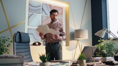 İnternetteki toplantıda iş adamı konuşuyor. Ofiste dizüstü bilgisayarın önünde duruyor. Ciddi sakallı CEO video konferansı düzenleyip iş belgelerini okuyor. Sakallı, orta yaşlı, kendine güvenen patron web kamerasıyla konuşuyor..