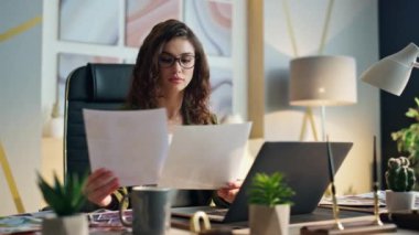 Genç bayan girişimci şirket ofis masasında oturan kağıtları analiz ediyor. Çekici, ciddi iş kadını işine odaklanmış. Akıllı ciddi kız yönetici iş yerinde tasarım örnekleri tutuyor..