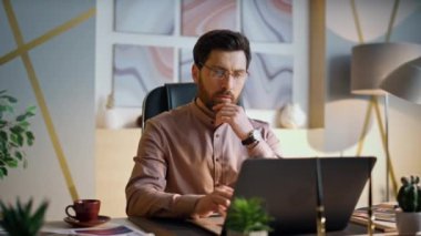 Ofiste çalışan odaklanmış sakallı bir iş adamı laptopa yakından bakıyor. Modern işyerinde klavyede oturan kendinden emin bir şirket yöneticisi. Orta yaşlı girişimci düşünce iş sorunları.