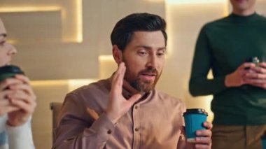 Kahve molasında konuşan dost canlısı şirket çalışanları modern ofis yerlerini kapatıyorlar. Mutlu sakallı yönetici, komik hikayeleri olan meslektaşlarını eğlendiriyor. Yaratıcı ekip gayri resmi iletişimin keyfini çıkarıyor.