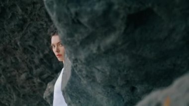 Yakın plan, beyaz seksi mayo giymiş çekici bir kadın Cliff 'in yanında poz veriyor. Deniz kıyısında taş kayalara yaslanmış seksi bir modelin portresi. Genç ve güzel kız kameraya özgüvenle bakıyor..