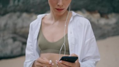 Modern kulaklık takan sakin genç bir kadın kumlu tepenin önünde dikiliyor. Açık havada müzik dinleyen çekici barışçıl kız. Rahat bayan cep telefonu uygulamasında favori şarkının tadını çıkarın..