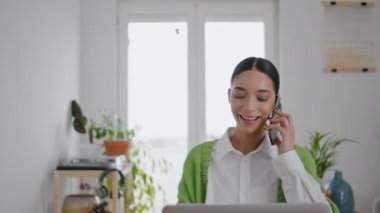 Bilgisayardaki akıllı telefonlara cevap veren mutlu model. Pozitif zeki kız cep telefonu dinlerken tek başına. Masada çalışan cep telefonuyla konuşan genç bir kadın.