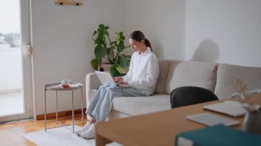 Öğrenci kız laptopla iş birliği yapıyor. Çevrimiçi yazı yazmayı öğrenen odaklı bir kadın iç kısımda beyaz renklerde. Bilgisayar başında çalışan zeki bir kadın kanepeye bağlanmış hissediyor. Uzaktan eğitim kavramı