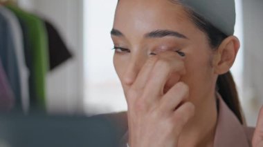 Ciddi bir bayan eve yakın çekim yaparken takma kirpik takıyor. Makyajdan zevk alan odaklanmış kadın yüzü odada güzellik rutini yapıyor. Esmer blogcu kız internette abonelerle konuşuyor.