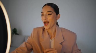 Blogcu kız kapalı mekanda cep telefonu kullanarak makyaj dersini kaydediyor. Nüfuzlu bir kadın cep telefonu kamerasına bakıyor ve evinde profesyonel ışıkla canlı yayın yapıyor. Kozmetik ürünleri incelemesi 