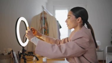 Stüdyoda cep telefonunu çeviren nüfuzlu bir kız. Güzellik blogcusu cep telefonunun yerini değiştiriyor. Akıllı telefon ekranı görüntüsü olan odaklanmış kadın beyaz dairede özel ders kaydı yapıyor. 