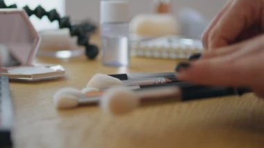 Masada makyaj fırçalarını sıralayan kadın elleri. Kadın parmakları evde tek başına makyaj malzemelerini inceliyor. Bilinmeyen kız ahşap masa içinde güzellik prosedürlerine hazırlanıyor. Günlük rutin kavram