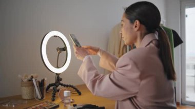 Blogcu kadın üç ayaklıya akıllı telefon takıyor. Video blogu için cep telefonu hazırlama ekipmanlarını ayarlayan modern bir etkili. Makyaj dersini kaydeden kız. Kozmetik ana sınıfı. 