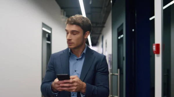 stock image Serious employee texting smartphone in office. Confident businessman using phone leaving contemporary business center. Handsome executive greeting colleagues checking emails making arrangements.