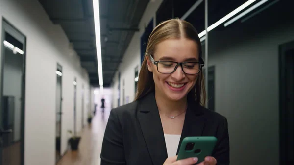 Happy businesswoman checking smartphone email. Smiling manager make yes gesture reading good news. Successful trainee rejoicing using mobile phone on go. Beautiful office employee get job promotion.