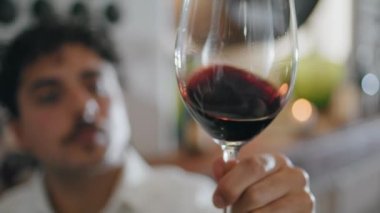 Genç adam şeffaf bardakta dönen kırmızı şarap kaliteli üzümlü alkolü yakından kontrol ediyor. Profesyonel üzüm bağı uzmanı şeffaf kadehleri sallıyor. Renkli içeceği test ediyor. Şarap yapımı konsepti.