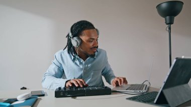 Kulaklıkçı adam kontrol odasını kullanıyor. Afrika kökenli Amerikalı müzik yapımcısı Midi klavyesine dokunuyor. Ses ekipmanlarıyla çalışan ciddi bir düzenleyici ev stüdyosunda şarkılar yaratıyor. 