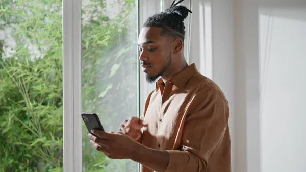 Serious freelancer virtual call mobile near window closeup. African american guy explaining using video chat. Handsome man talking cellphone at home. Smart student online smartphone conference