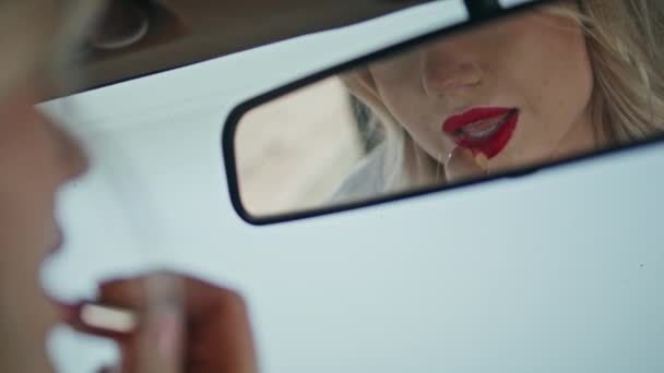 官能的な唇に赤い口紅を適用する美しい女性を反映した車のミラーを閉じます 自動車の中に座って化粧を作る豪華なブロンド 若いです魅力的な女の子見ます上の顔の美しさ反射 — ストック動画