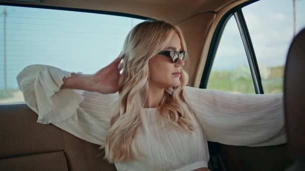 エレガントなサングラスをかけて車の後部座席に座って豪華な女性の乗客 外では車の窓を見ている魅力的なリラックスした女の子 ゴージャスブロンドライドでレトロな自動車閉じるアップ — ストック動画