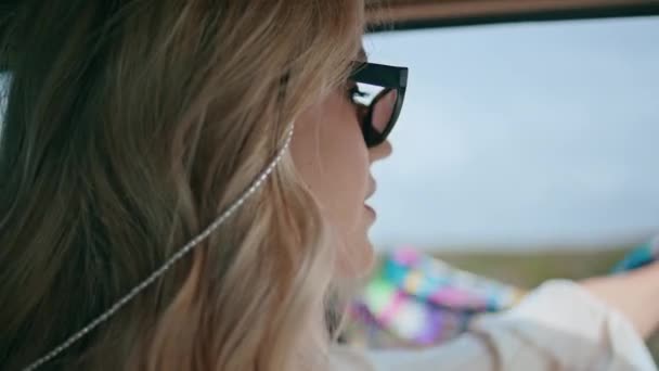 オープンカーの窓で風でスカーフを保持する幸せな女の子のドライバを閉じます サングラスの中で魅力的な屈託のない女性は笑顔高速道路で高速運転をお楽しみください 自動車に乗る肖像画美しい陽気な旅行者 — ストック動画