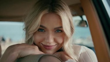 Kameraya yakından bakan gülümseyen bir kadın. Retro otomobilde poz veren güzel, şehvetli sarışın portresi. Sevimli mutlu gezgin kız hafta sonu otomobil yolculuğunda dinleniyor. Trip konsepti.