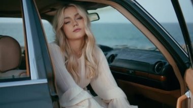 Araba gezisinde dinlenen bir kız deniz kıyısında yolcu koltuğunda eski bir otomobilde oturuyor. Çekici, kendine güvenen bir kadın. Arka planında güzel bir okyanus olan klasik bir araçta poz veriyor. Deniz yolculuğu konsepti.