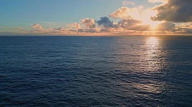 Dalgalanan okyanus yüzeyi güzel günbatımını yansıtıyor. Karanlık deniz suyunda yavaş çekim parlayan parlak altın ışınlar ile hava manzaralı deniz gündoğumu. Gün batımı bulutların arasından doğan güneş ışığı.