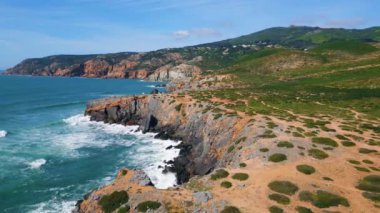 Güzel deniz manzaralı güneşli kayalık kıyı şeridi derin mavi okyanus suyuyla yıkanıyor. İnsansız hava aracı manzaralı köpüklü deniz dalgaları yavaş çekimde kıyı taşlarına sıçrıyor. Sinematik küçük doğa yaz günü..