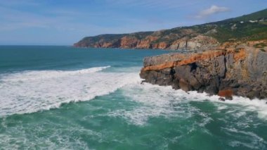 Çarpıcı deniz engebeli sahil kayalıklarına çarpıyor. Güzel güneşli bir gün, ağır çekimde. Hava dalgaları volkanik kayalara yuvarlanıyor. Deniz köpüğü köpürüyor. Martı fırtınalı turkuaz dalgalar üzerinde uçuyor..