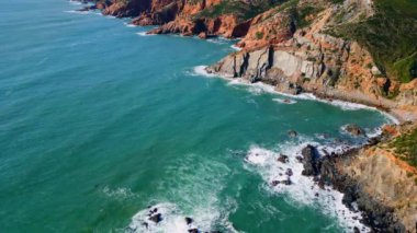 Sinema manzaralı kayalık sahil sakin mavi okyanus suyuyla yıkanıyor. Hava manzaralı güzel deniz dalgaları taşlı kıyı şeridine yuvarlanıyor köpükler yavaş çekimde sıçrıyor. Fırtınalı dalgalar engebeli kayalıklara çarpıyor.