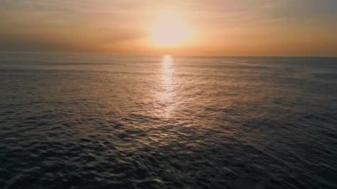 Sabah deniz dalgaları yavaş çekimde sıçrıyor. Güneşin doğuşuyla dalgalanan deniz dalgaları, hava görüntüsünü yakınlaştırır. Turuncu güneş ışınlarının altında yüzen manzaralı derin su. Karanlık okyanus yüzeyi pastel ışığı yansıtıyor. 