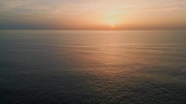 Okyanus yüzeyi güneşi yansıtıyor. Süper yavaş çekim. Güneşin doğuşuyla dalgalanan deniz dalgaları. Turuncu gökyüzü ufkuna uzanan manzaralı derin su. Koyu deniz gelgiti Pastel ışıkta ilerliyor