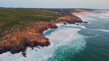 Turkuaz okyanus dalgaları sabah deniz manzarası yavaş çekimde kayalık kıyılara vuruyor. Hava sineması köpüklü deniz suyu sahil kayalıklarına çarpıyor. Panoramik deniz manzarası taş deniz kıyısı