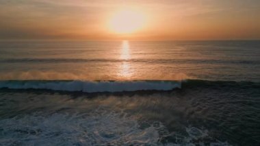 Güneşin doğuşu deniz sörfü plaj drone görüntüsünü yıkıyor. Karanlık, sakin okyanus yüzeyinde altın şafak gökyüzü. Gün batımında ağır çekimde hareket eden huzurlu dalgalar. Meditasyon yapan sakin deniz manzarası 