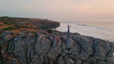 Gezgin, günbatımı okyanusunun fotoğrafını çekiyor. Panoramik manzara gezgini, cep telefonuyla Pastel Ufuk 'u filme çekiyor. Sakin deniz dalgaları parlak güneşi yansıtıyor. Deniz doğası