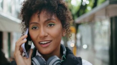 Rahat Afro-Amerikan kadın cep telefonuyla konuşuyor. Şehir caddesinde yürüyor. Yaklaş. Havalı kıvırcık kız turist dışarıda dolaşırken telefon görüşmesini bitirdi. Çekici bayan iletişim için hücreyi kullanıyor..