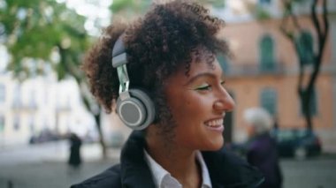 Modern kulaklıklarla müzik dinleyen mutlu bir kız. Şehir caddesini kapatıyor. Kablosuz kulaklıkla favori müzikten hoşlanan neşeli Afro-Amerikan kadın portresi. Hipster hanım seviniyor.