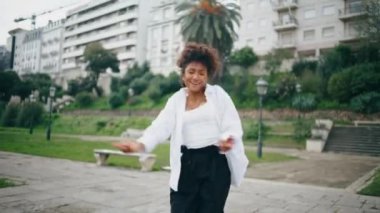 Neşeli kadın dansçı şehrin sokaklarında serbest stil performansının tadını çıkarıyor. Yetenekli Afrikalı Amerikalı kız sanatçı modern tarz dansı yapıyor. Kıvırcık enerjik sanatçı ritmik olarak ağır çekimde hareket ediyor.