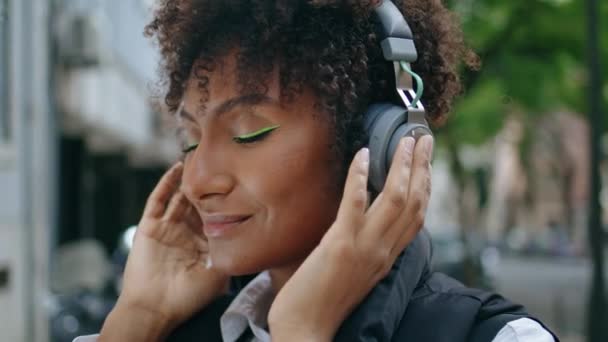 이현대적 머리장식의 아름다운 음악을 아프리카 미국인 여자가 헤드폰을 거리에서 소리를 — 비디오