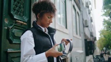 Kablosuz kulaklık takan Afro-Amerikan kadın caddeyi kapatıyor. Kendine güvenen güzel kız açık havada müzik dinlemek için moden kulaklık takıyor. Şık bir bayan cep telefonunda uygulama açıyor