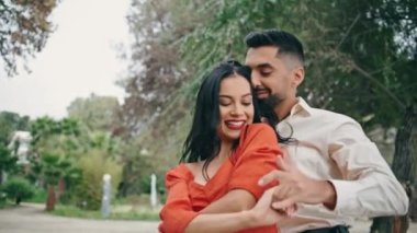 Şehir parkında seksi Latin dansı yapan mutlu şehvetli partnerler. Genç, gülümseyen bir adam tutkulu salsa sosunda esmer bir kadına sarılıyor. Heyecanlı İspanyol çift açık havada gösterinin tadını çıkarıyor..