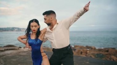 Kasvetli deniz kıyısında tango yapan seksi profesyonel sanatçılar. Odaklanmış tutkulu dansçılar bulutlu zeminde seksi Latin koreografisi yapıyorlar. Güzel bir çift, duygusal performansı yavaş çekimde sever.