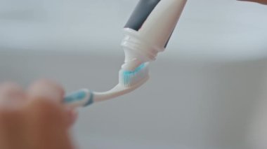 Kapalı alanda fırçaya diş macunu süren kadın eli. Bilinmeyen bir kadın sabah banyosunda diş fırçalamaya hazırlanıyor. Kimliği belirsiz bir kız tüpü tutuyor. Diş sağlığı ve günlük sağlık hizmetleri
