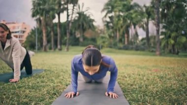 Spor yapan kadın, tropikal doğada egzersiz yapıyor. Atletik kız en iyi arkadaşıyla yoga minderinde kol egzersizi yapıyor. Kasvetli bir günde iki aktif bayan güç uygulaması. Sağlıklı yaşam tarzı kavramı